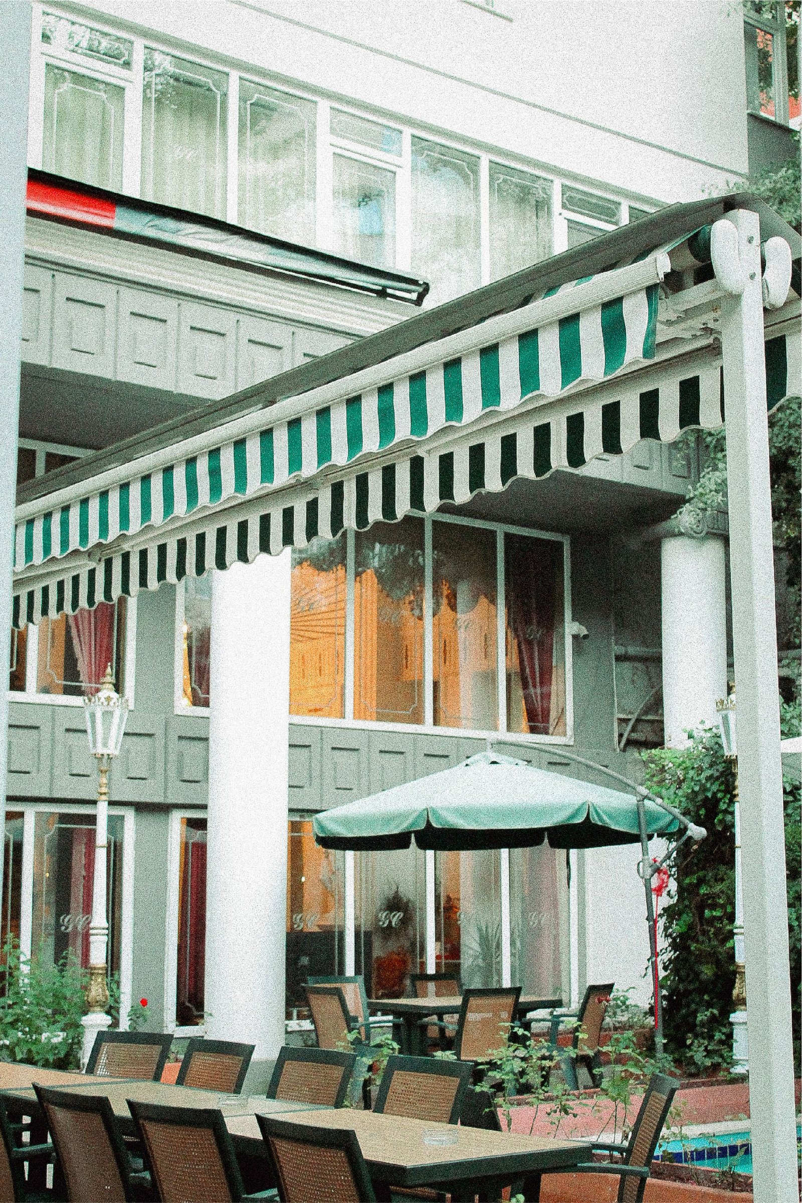 Echt restaurantterras met tafels en stoelen onder een gestreepte luifel.