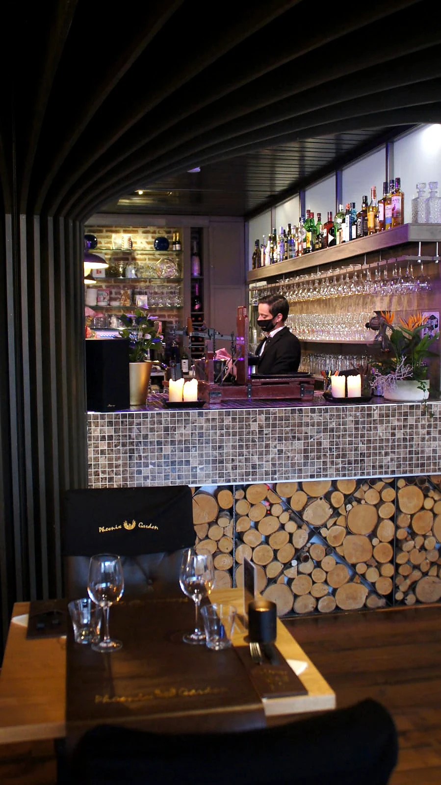 Bar en servicepunt van Phoenix Garden met medewerker, glaswerk, kaarslicht en houtdetails.