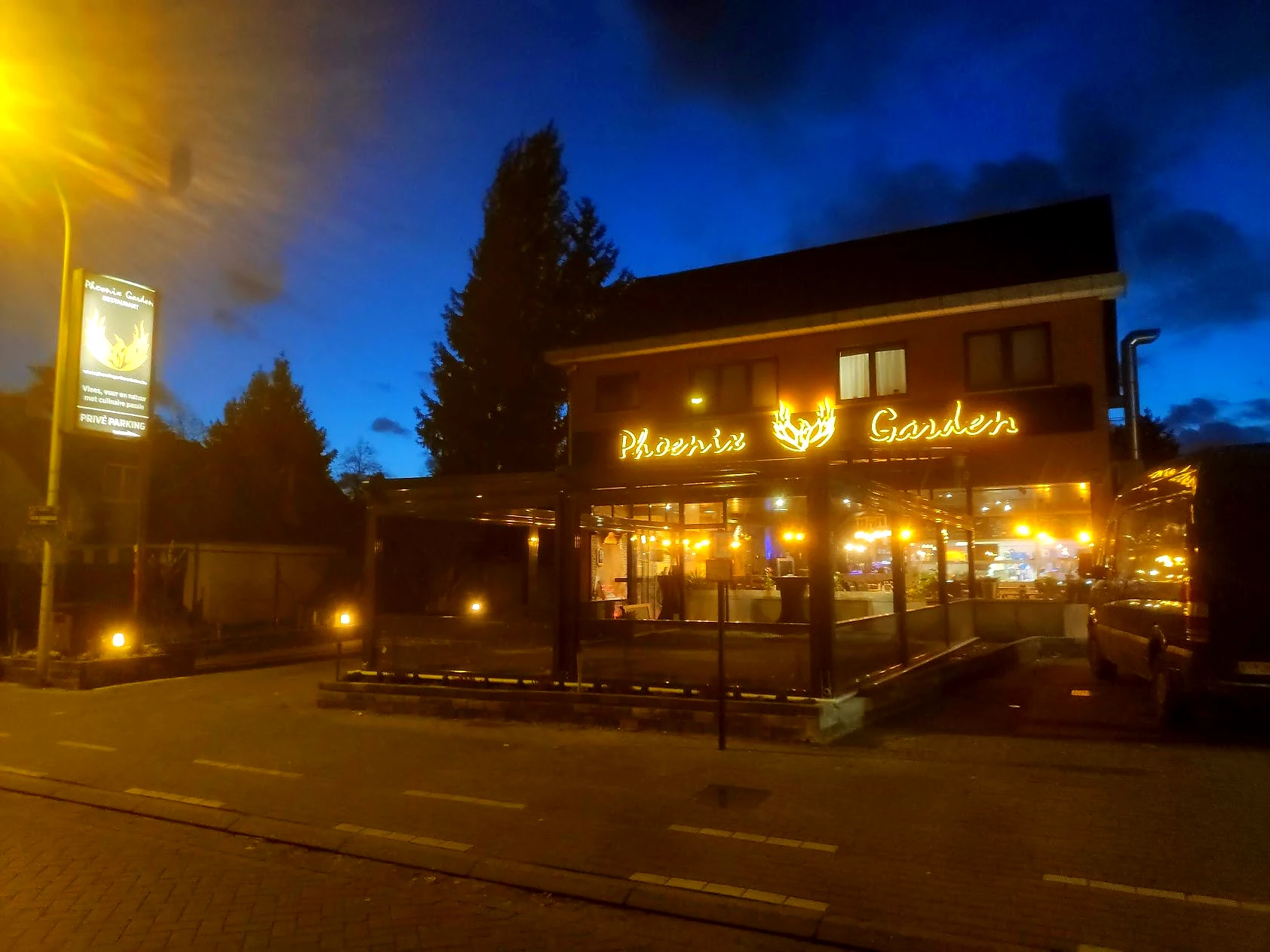 Phoenix Garden aan de straat in de avond met warme lichtsigning op de voorgevel.