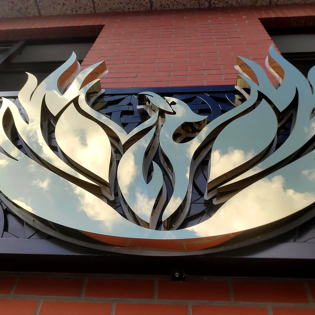 Detail van het metalen Phoenix Garden-logo op de bakstenen gevel.