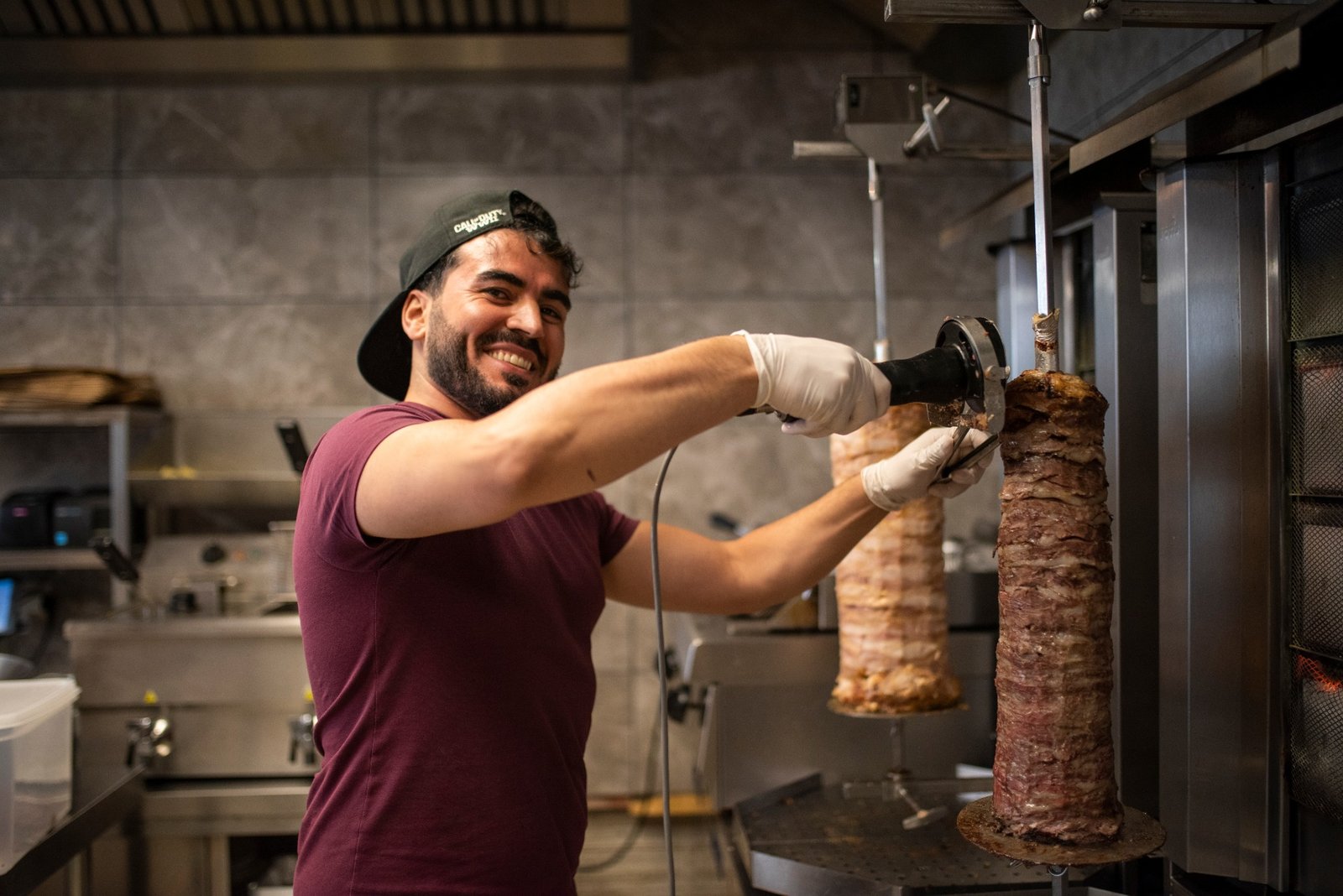 Lachende medewerker snijdt verse döner van het spit in de keuken van Topkapi.
