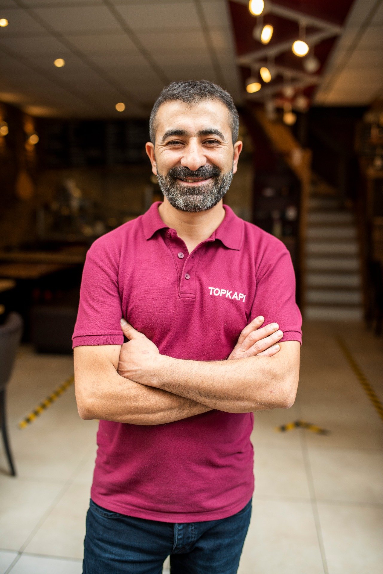 Portret van Ferdi, eigenaar van Topkapi, in een bordeauxrode polo voor de ingang van het restaurant.